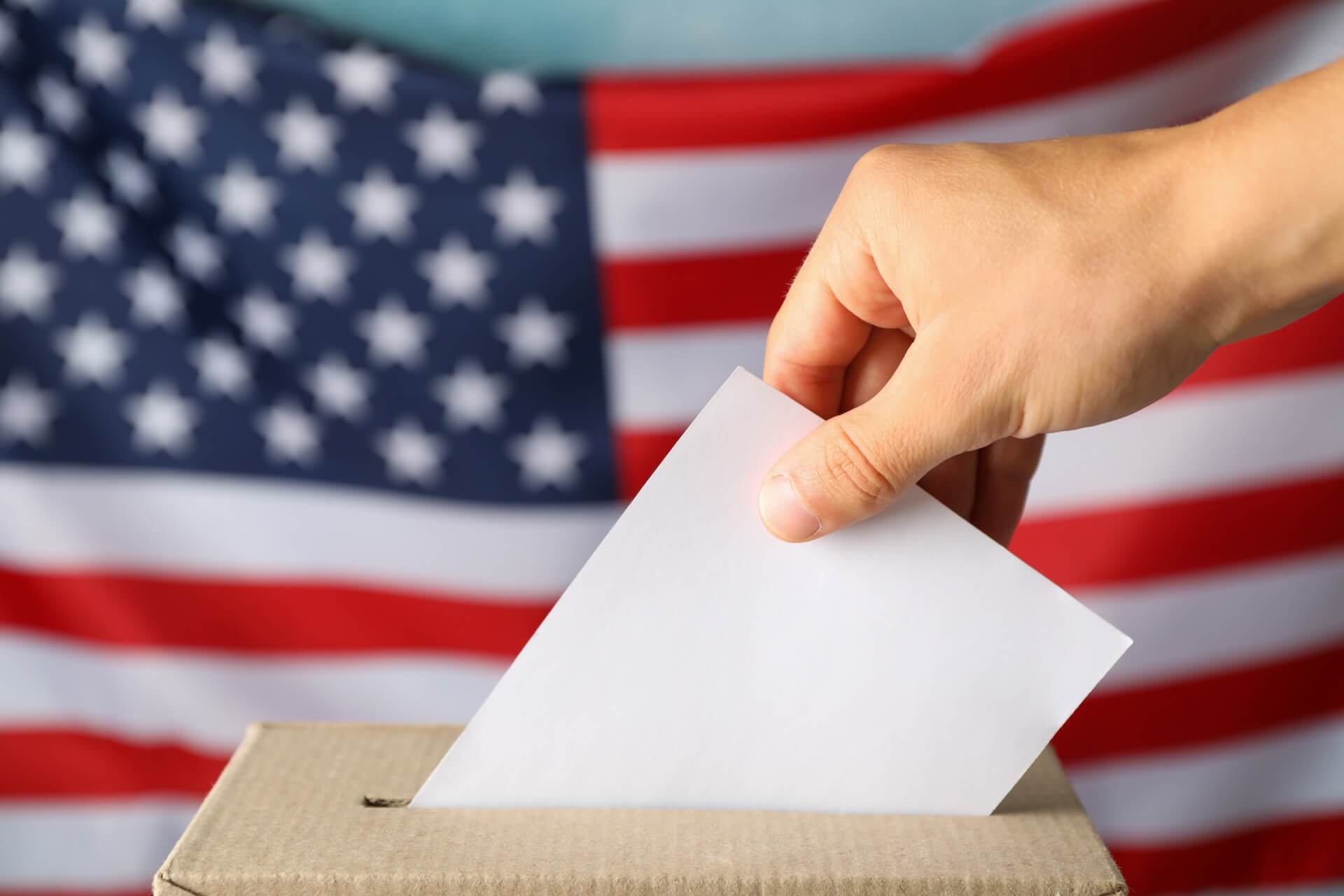man-putting-ballot-into-voting-box-against-american-flag